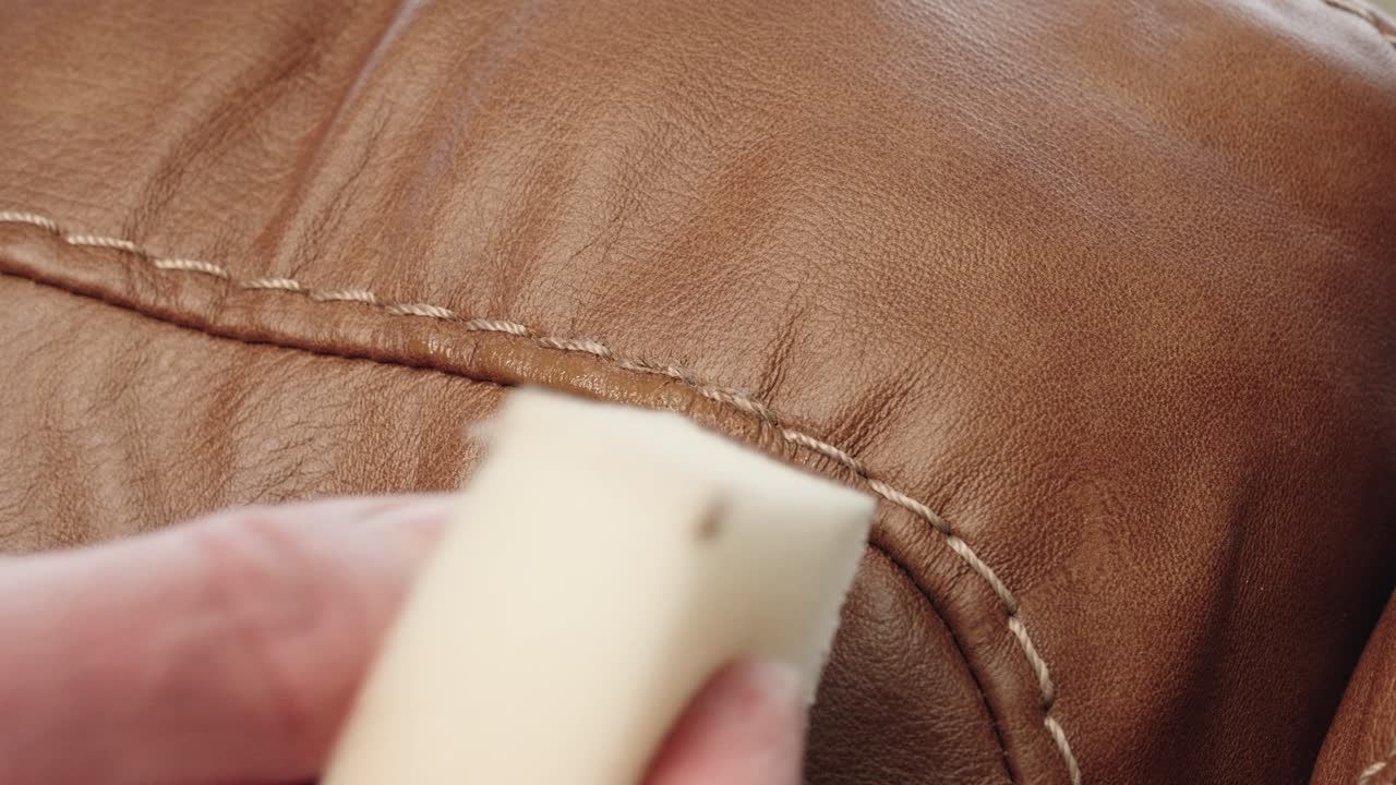 Hands delicately dab matching paint with sponge to erase sofa scratch completely