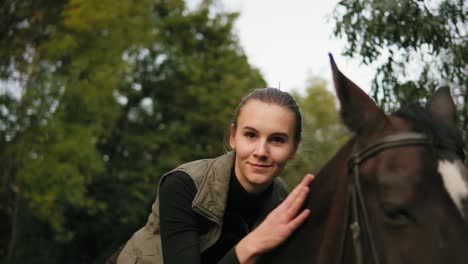 young beautiful woman stroking brown horse while sitting in the saddle and putting her head on the horse's head looking in the