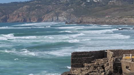 Langsame-Mo-Azurblaue-Wellen-Mit-Bergen-Im-Hintergrund,-Kap-Roca,-Portugal