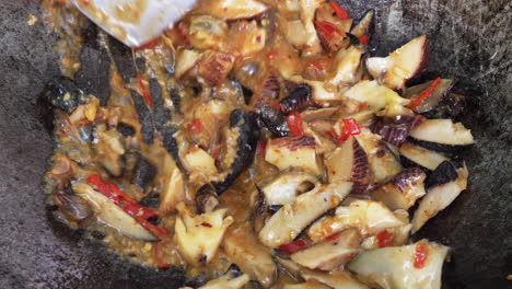 stirring stir fried sea snail dish in wok with spatula, close-up