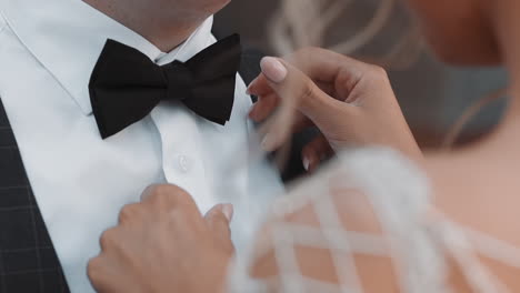 lady bride adjusts bow tie on neck of young groom at wedding