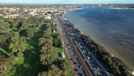 aerial top down: busy traffic on coastal road beside swan river in perth city at sunset - panning shot