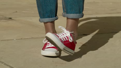 close-up de pés de mulher jovem feliz dançando e pulando usando tênis converse vermelho em um piso de concreto em um dia ensolarado