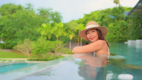 Side-view-of-a-young-woman-half-submerged-in-the-swimming-pool-water,-looking-at-the-camera-and-smiling