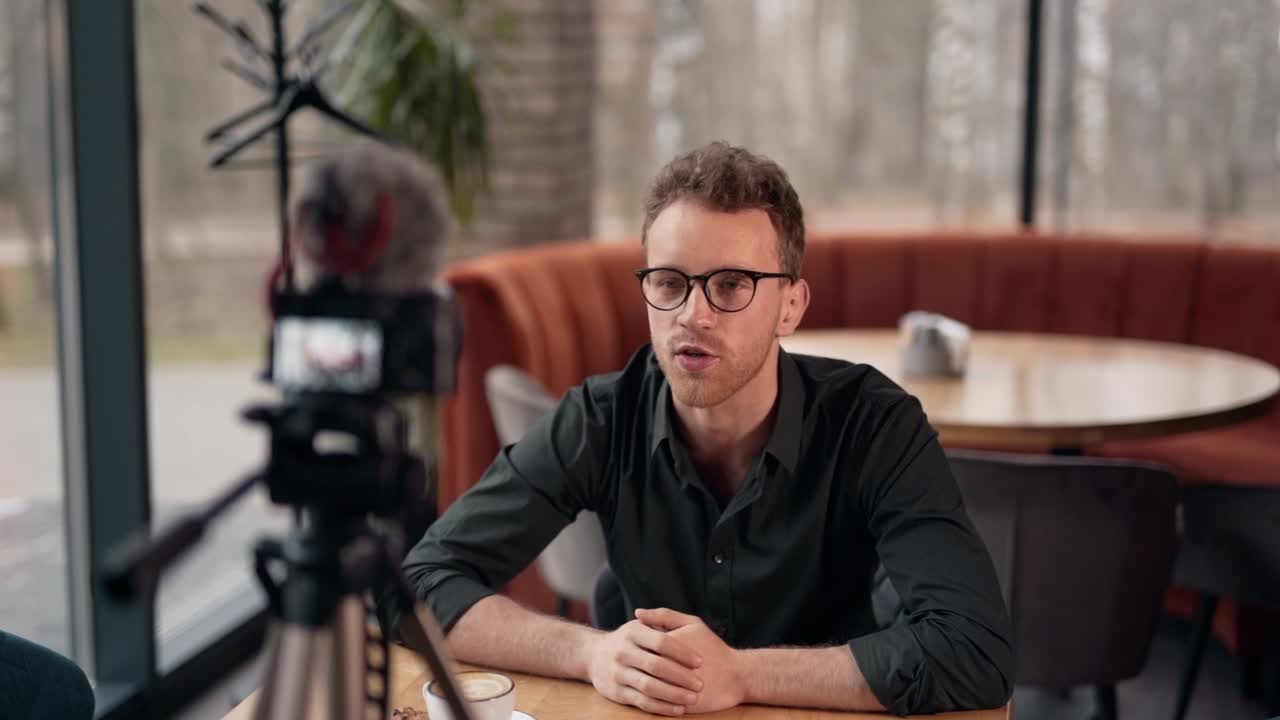 Charismatic handsome young man recording video on camera on a tripod in a cafe
