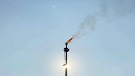 Polluting-Gas-Flare-industry-refinery-against-sun,-clear-sky,-zoom-in,-day