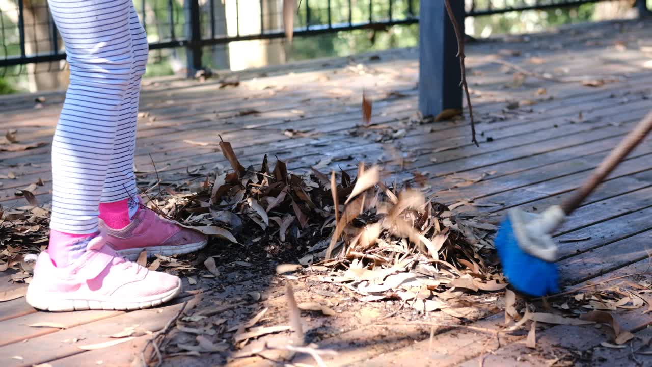 Two young girls doing household chores of sweeping the deck