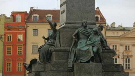 medium shot of monument sculptures with historical european buildings in the background. cracow main square, poland. adam mickiewicz statue krakow.