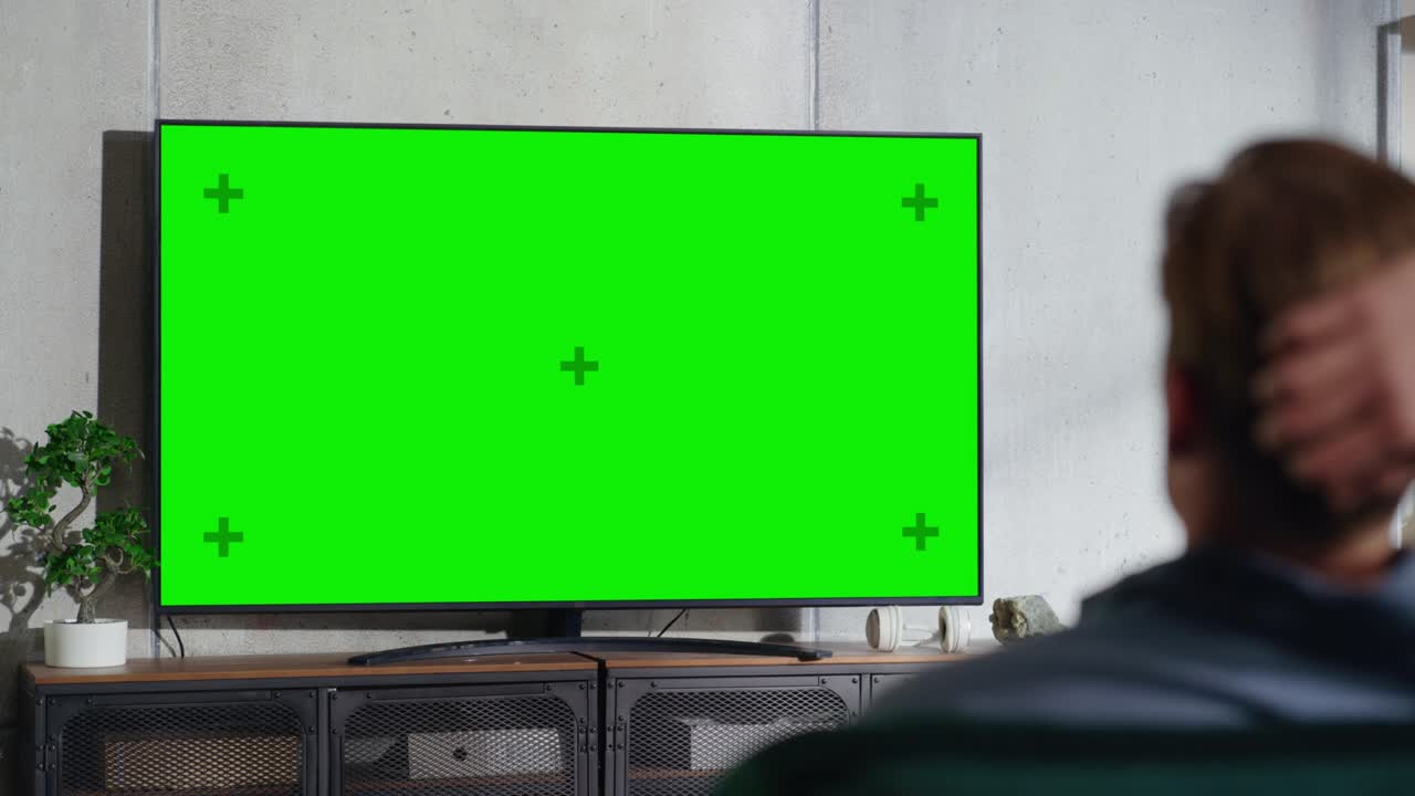 소파에 앉아서 수평 녹색 화면으로 tv를 보고 있는 젊은 멋진 남자, 그것은 집에서 방에서 낮 시간입니다.