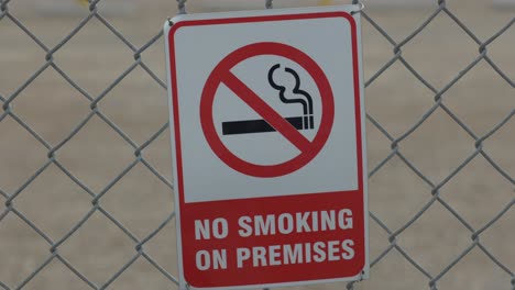 a quick zoom in on a red and white no smoking sign that is behind a chain linked fence