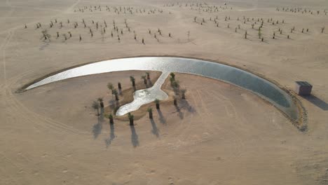 Aerial-view-of-the-Moon-Lake-in-Dubai,-Moon-Shape-Lake-is-in-the-middle-of-Al-Qudra-desert,-surrounded-by-golden-sand-dunes-in-the-United-Arab-Emirates