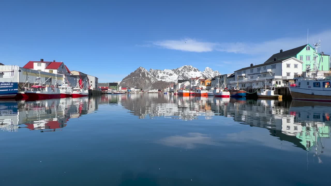 수면에 반사되는 건물과 보트가 있는 헤닝스베르 항구의 정적 샷, 배경의 아름다운 산, 로포텐 섬