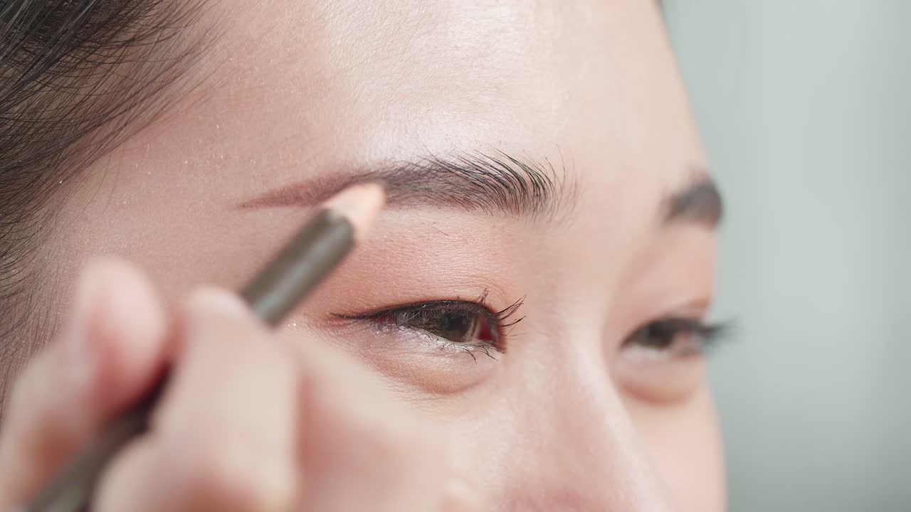 Close Up Of Beautiful Young Asian Woman Applying Eyebrow Pencil And Smiling While Applying Makeup At Home