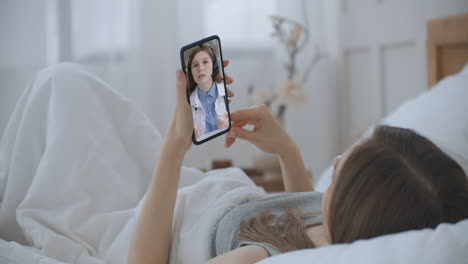Frau-Prüft-Mögliche-Symptome-Mit-Professionellem-Arzt-Per-Online-Video-Chat.-Junges-Mädchen,-Das-Zu-Hause-Krank-Ist,-Nutzt-Das-Smartphone,-Um-über-Eine-Videokonferenz-Medizin-App-Mit-Ihrem-Arzt-Zu-Sprechen.