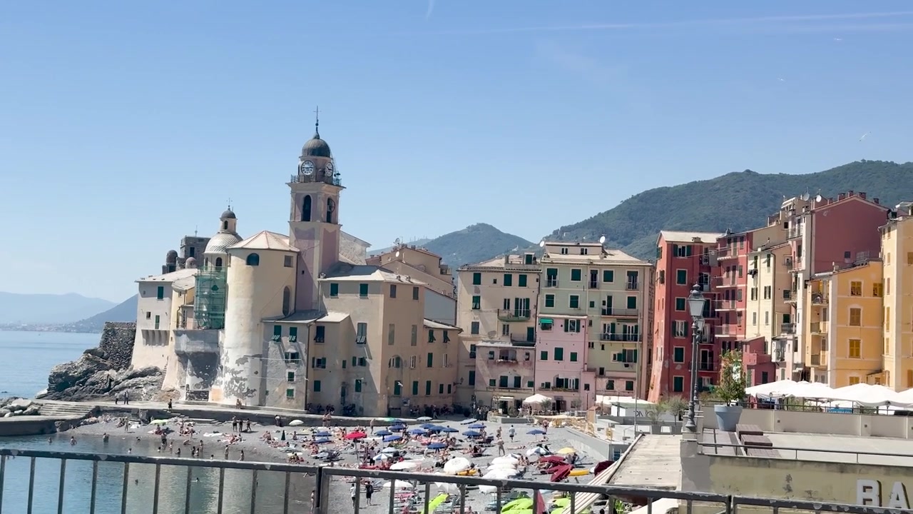 Una lenta panoramica cattura una vivace architettura costiera e una spiaggia affollata sotto la luce intensa del sole.
