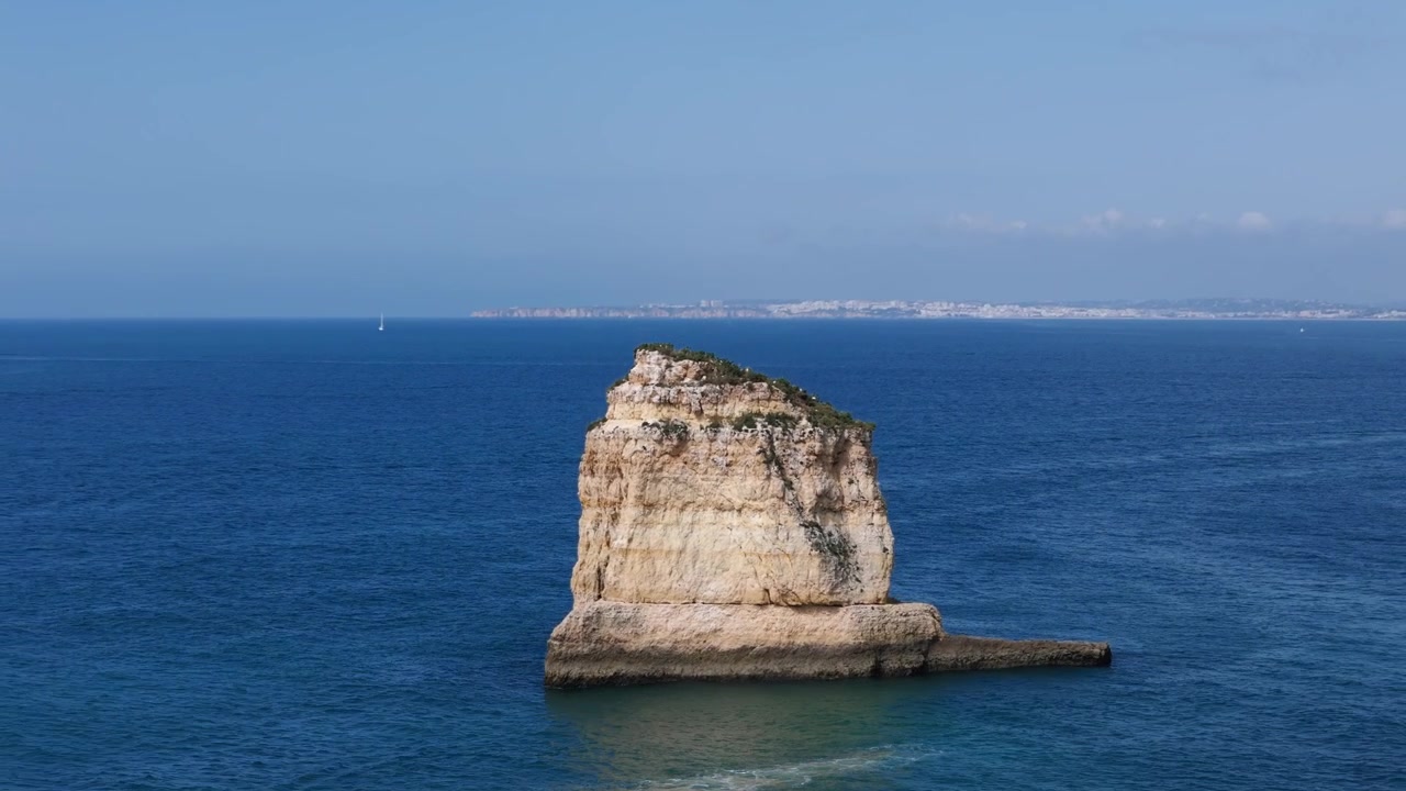 Ripresa aerea con drone in allontanamento da un'enorme roccia nell'oceano, che rivela l'oceano blu in Algarve, Portogallo.