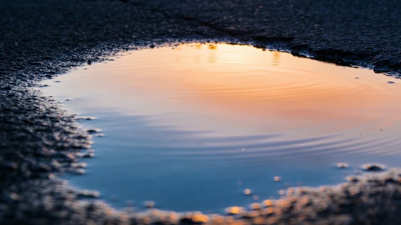 アスファルトの浅い水たまりに水滴が落ち、同心円状の波紋が立って空を映している。