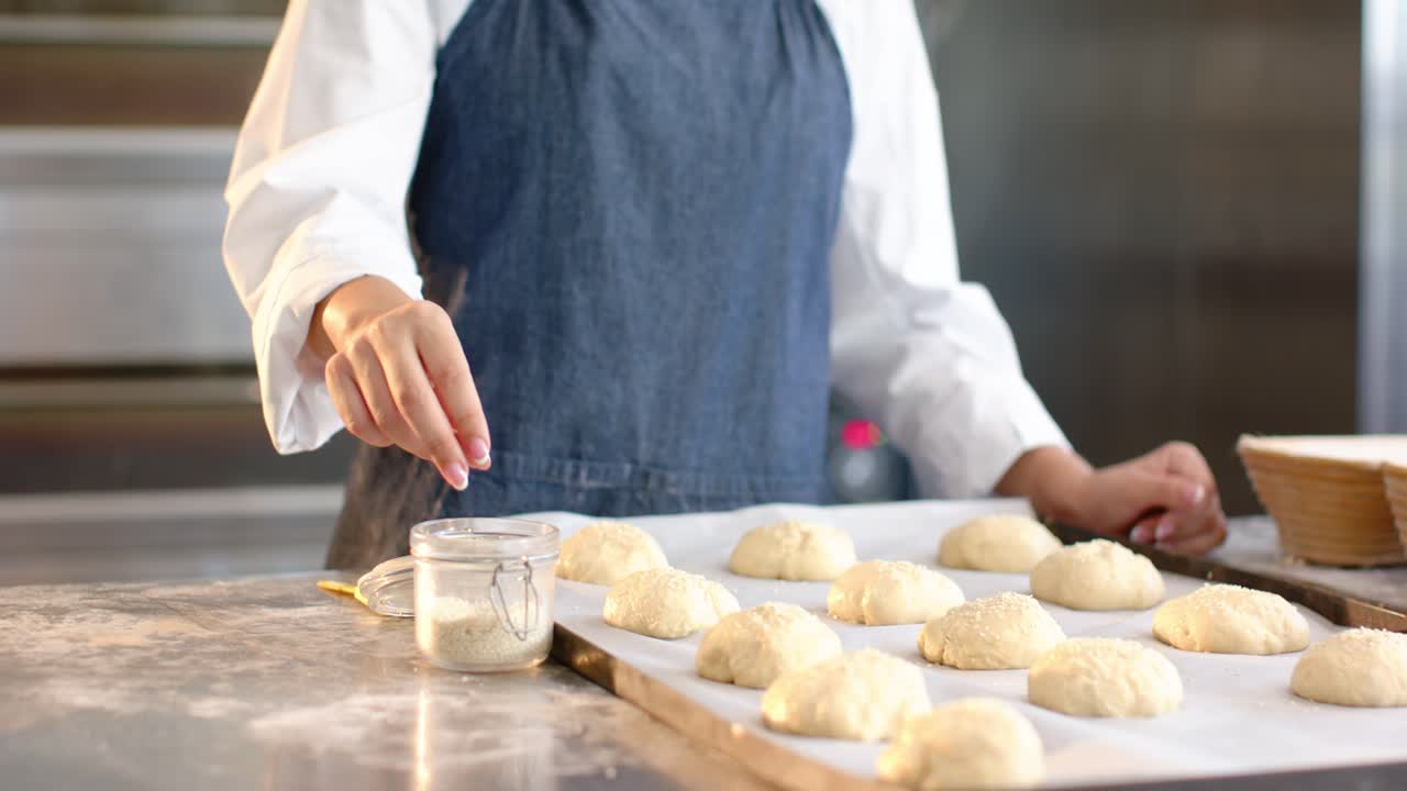 African American woman in denim-apron at work counter pinching first dipping into jar coating rolls
