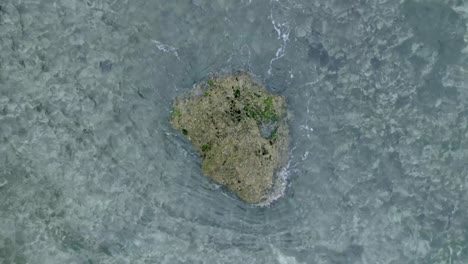 Top-Down-Slow-Motion-Drone-View-of-Waves-crashing-over-shallow-coral-reef-and-big-rock-in-Uluwatu-Bali-Indonesia