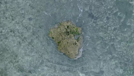 top down slow motion drone view of waves crashing over shallow coral reef and big rock in uluwatu bali indonesia
