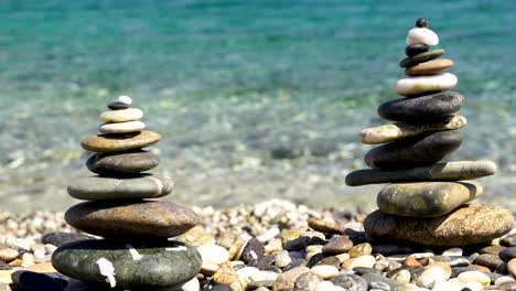 Zen-Gestapelte-Felsen-An-Einem-Strand-Mit-Kristallklarem-Wasser-Im-Hintergrund-In-Sardinien,-Italien