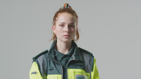 studio portrait of serious young female paramedic turning to face camera against plain background