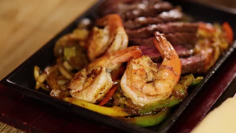 close-up of sizzling beef and shrimp fajitas served with sauce in a warm, inviting restaurant setting