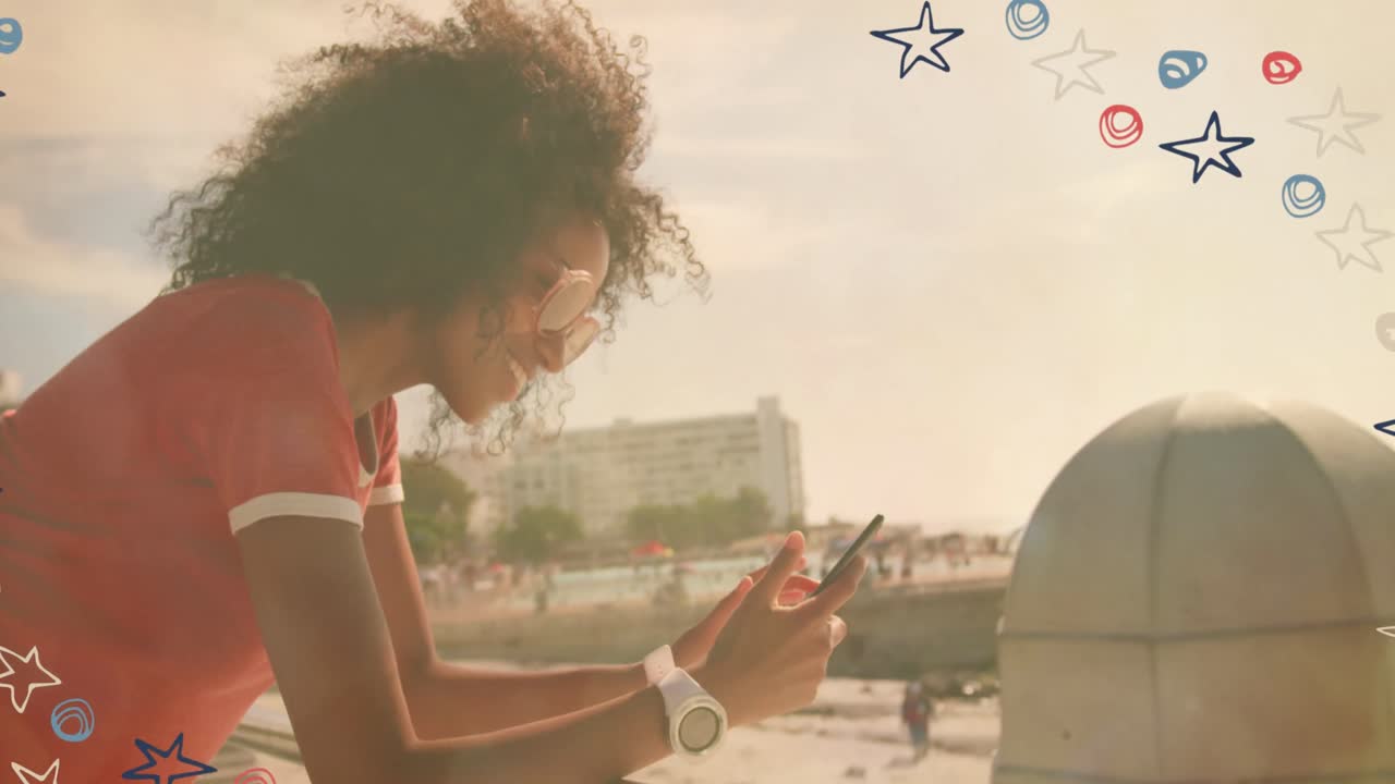 Colorful star icons against african american woman using smartphone near the beach