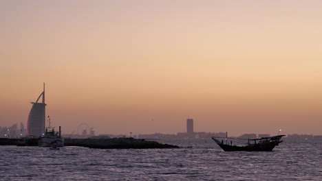 siluetas de dhow en el mar después de la puesta de sol con burj al arab en segundo plano.