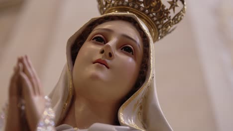 close up of crowned virgin mary statue with hands in prayer inside church