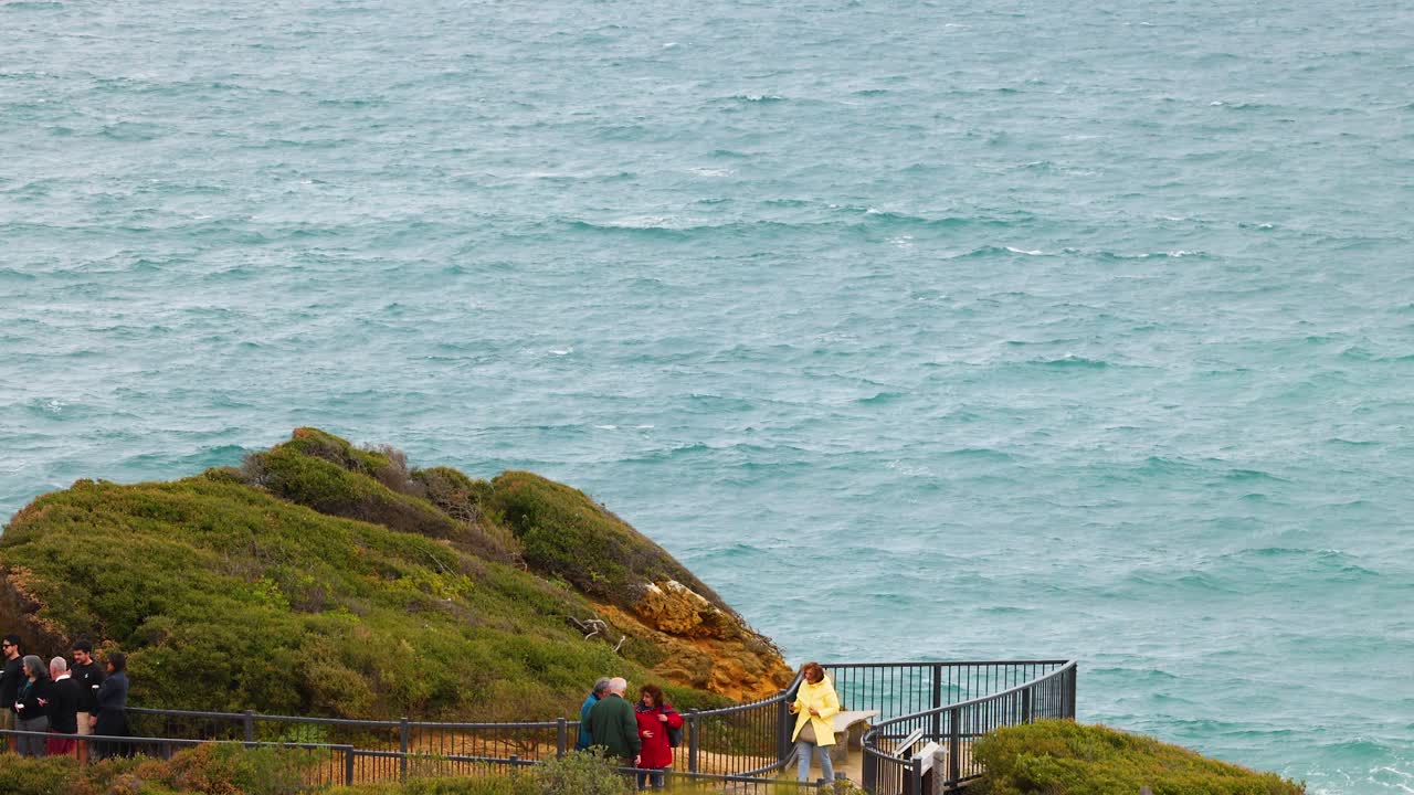 People enjoy a coastal view from a cliffside lookout on a cloudy day at Great Ocean Road, Australia