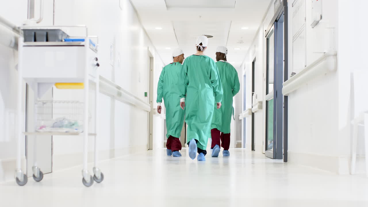 Diversi chirurghi e chirurghe in camice chirurgico camminano nel corridoio di un ospedale, al rallentatore.