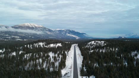 Luftaufnahme-Des-Cariboo-Highway-95,-Der-An-Einem-Bewölkten-Tag-Während-Der-Blauen-Stunde-In-Den-Horizont-Läuft,-Umgeben-Von-Beeindruckenden-Schneebedeckten-Bergen-Und-Wäldern:-Panoramaszene