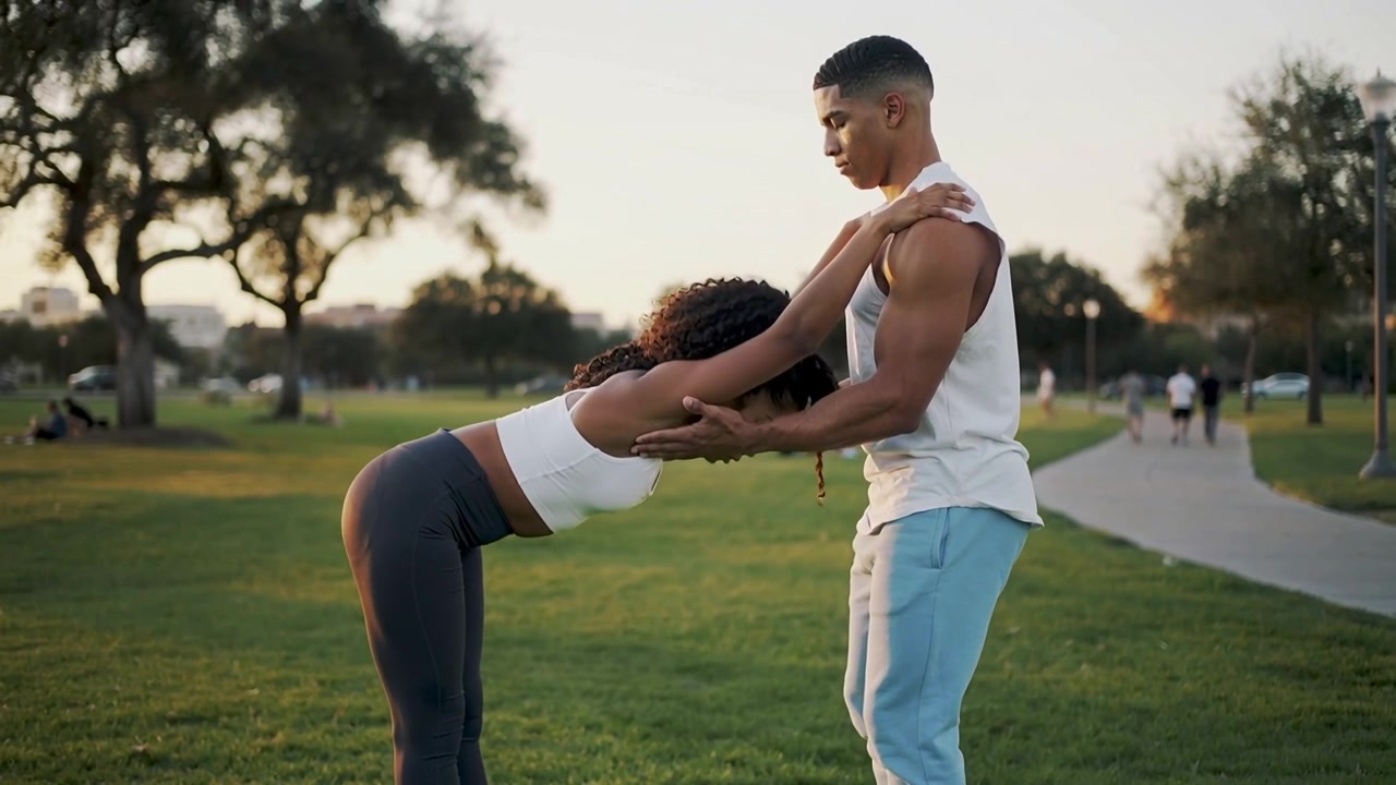 Duo che fa stretching si assiste a vicenda in un piegamento in avanti al parco, dopo aver unito le mani per la mobilità sui tappetini, in abbigliamento sportivo.