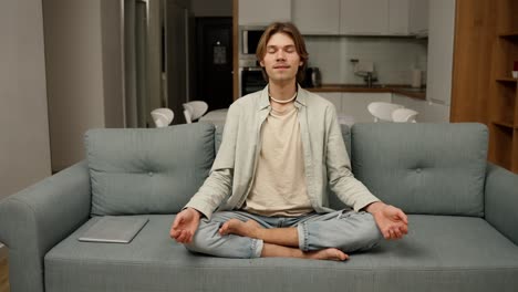 young man starts to meditate in his living room on the couch