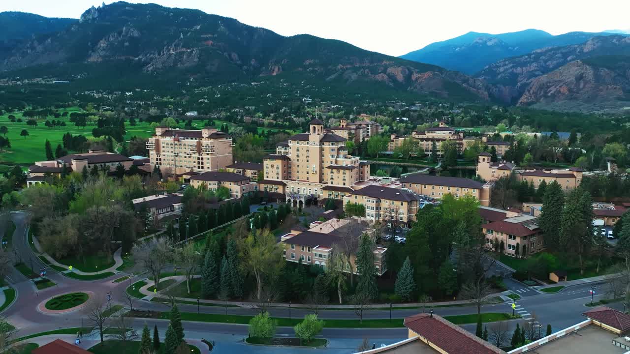 Wide aerial of angled establishing Broadmoor resort surrounded by trees and landscape, clear skies above with mountain backdrop