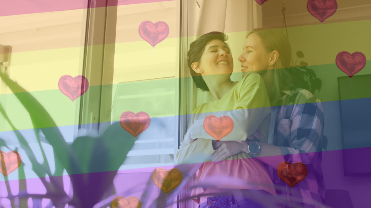 animación de emojis de corazón y bandera del arco iris sobre una pareja de mujeres caucásicas abrazándose