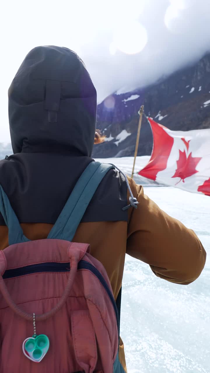 Una persona de pie sobre un glaciar con una bandera canadiense