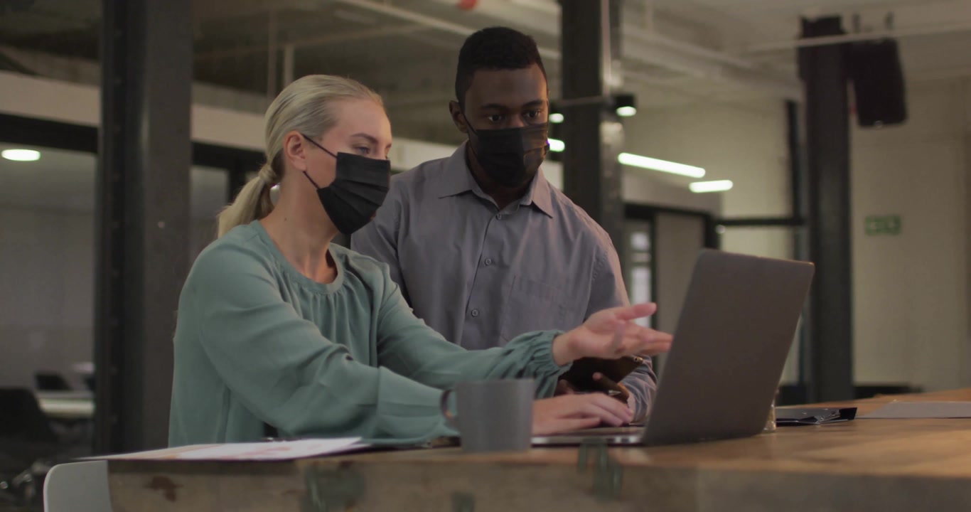 Woman typing on laptop in tech hub generating numeric ring while coworker referencing smartphone