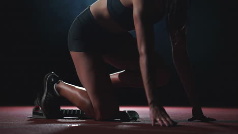 slender young girl in track and field is getting ready to start in the race in the running pads on a black background