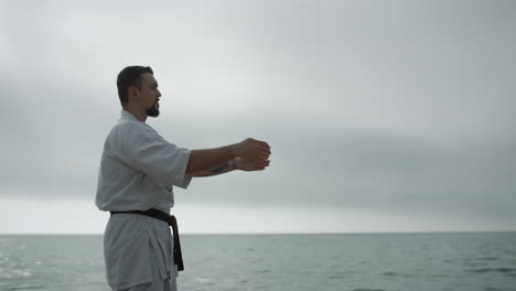 un deportista barbudo practicando artes marciales de pie en la playa. un hombre aprendiendo karate.