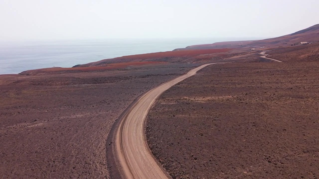 Vista Aérea de uma Estrada de Terra Sinuosa ao Longo de uma Costa Vulcânica
