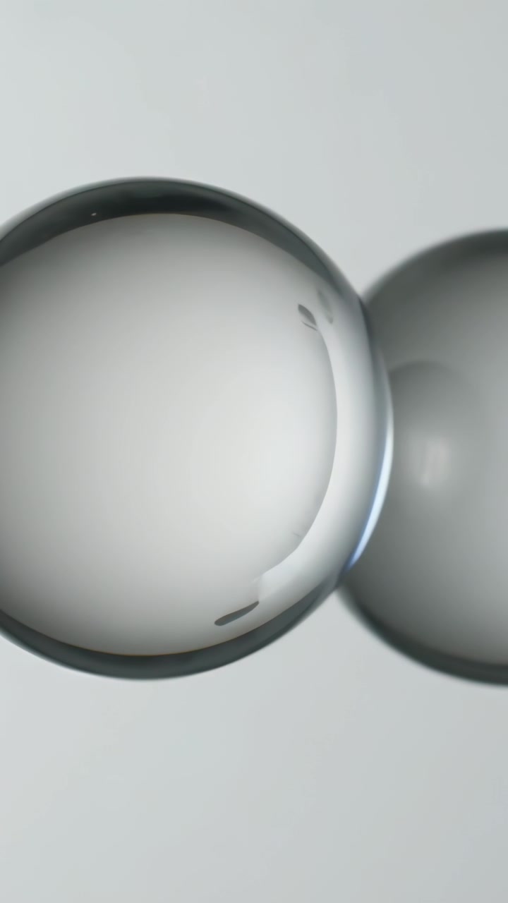 Vertical video: Drifting large glass sphere nudging right soft sphere in studio shifting glints