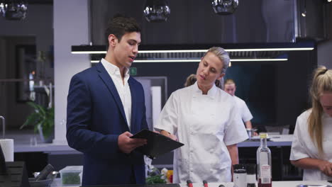 gerente de restaurante caucásico en la cocina hablando con una cocinera caucásica, dando instrucciones