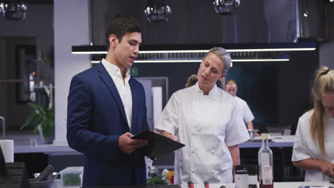 caucasian male restaurant manager in the kitchen talking to a caucasian female cook, giving instruct