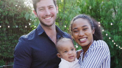 Portrait-Of-Loving-Parents-Holding-Baby-Daughter-At-Home-Outdoors-In-Garden