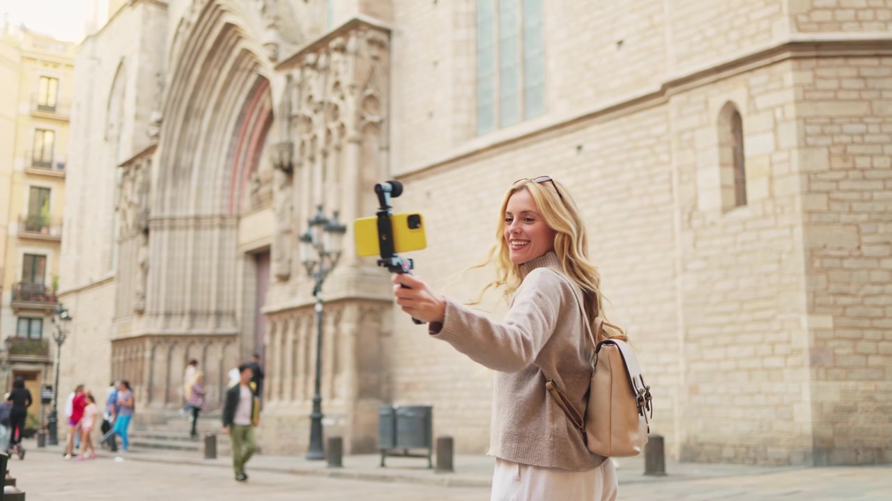 Donna bionda felice che fa vlogging con smartphone in una città europea