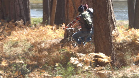 Couple-talk-as-they-ride-mountain-bikes-in-forest,-tight-pan