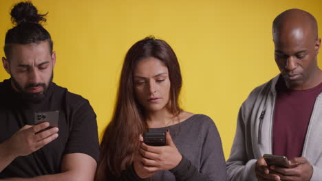 Fotografía-De-Estudio-De-Un-Grupo-De-Amigos,-Todos-Mirando-Sus-Teléfonos-Móviles-Contra-Un-Fondo-Amarillo.