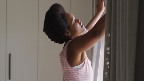 Happy-african-american-woman-widening-curtains-in-bedroom